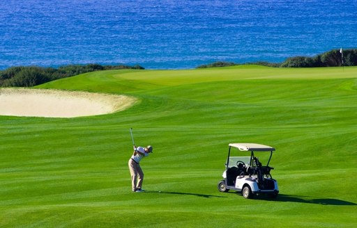 Golfer taking a swing towards the ocean at San Lorenzo Golf Club, Algarve
