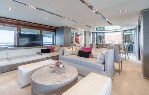Main salon onboard charter yacht BLISS, plush lounge area in the foreground with a dining table visible in the background