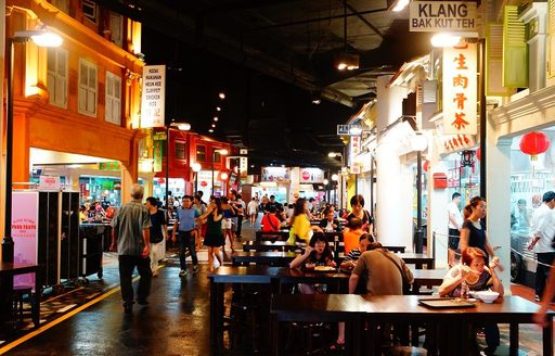Visitors enjoying local Malaysian food seated at wooden tables outside macan food stalls