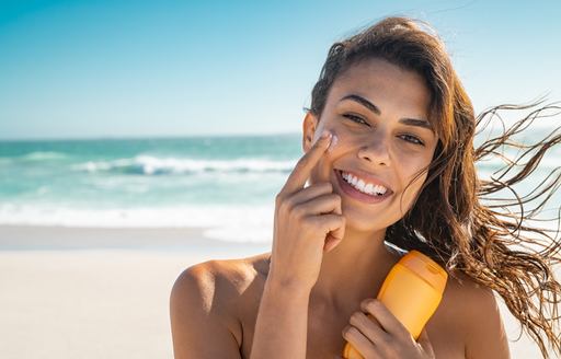 A smiling woman applies suncream against a beach backdrop
