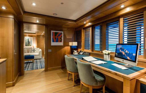 Office onboard charter yacht AIFER, desk to starboard underneath slatted windows with a lounge area visible through doorway in background.