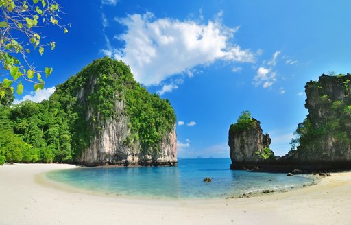 secluded Thailand beach with white sand, blue water and tall rock formations