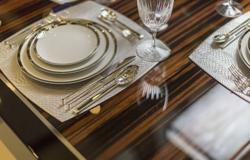 A wooden table laid up with bone china dishes with gold trim and respective cutlery for the various courses being served