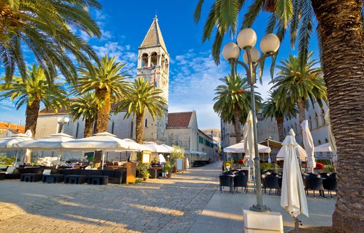 Main square in Croatia, with palm trees surrounding and stone chapel overlooking he central cafe