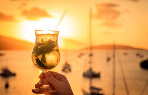 Woman holds cocktail with sunset in the Caribbean, BVIs