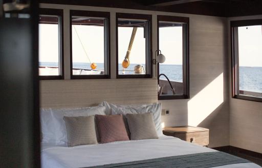 Cabin onboard charter yacht VELA, central berth facing forward with surrounding windows aft and to the side.