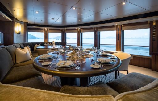 Interior dining area onboard superyacht charter OCTOPUS, circular table and bench seating surrounded by large windows