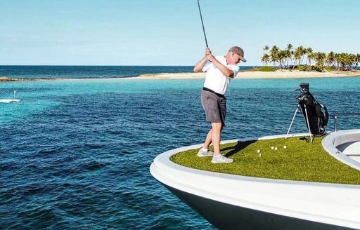a man swings his golf club from the bow of his luxury charter yacht during his social distancing vacation in the caribbean 