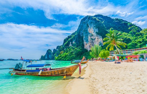 little wooden boat on the sand in south east asia, with mountain backdrop