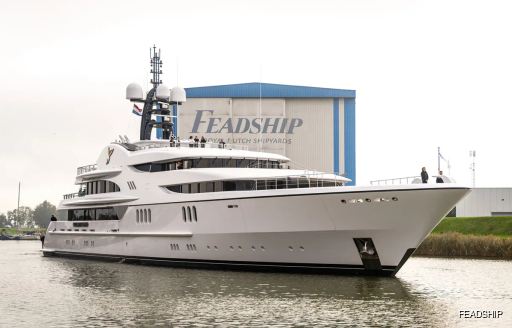 Charter yacht FIREBIRD leaving construction yard with Feadship logo in background