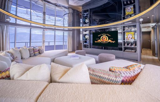 Upper deck salon onboard charter yacht FORTUNA, plush seating surrounding a large wall-mounted TV and full height windows in the background