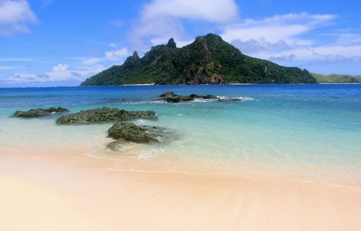 white sand beach with crystal waters and views of rugged island in Fiji