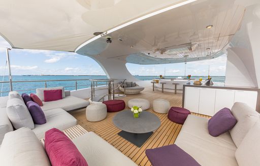 Overview of the sun deck onboard charter yacht BIG SKY, ample seating arranged in a U shape with purple cushions