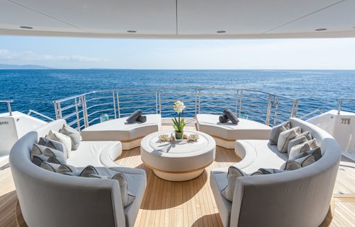 Overview of the aft deck onboard charter yacht THUMPER, curved seating and sun pads surround a coffee table