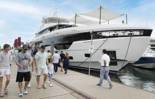 A motor yacht berthed at the Miami International Boat Show, with visitors walking by.