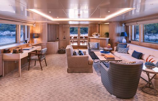 Overview of the main salon onboard charter yacht NATALIA V, extensive lounge area with neutral-toned seating surrounded by windows to both port and starboard