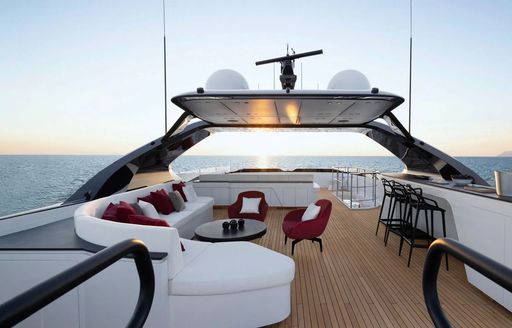 Overview of the flybridge onboard charter yacht N1, alfresco lounge area with plush white seating to port with a wet bar starboard