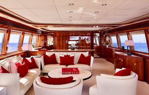 Main salon onboard charter yacht CHAMPAGNE AND CAVIAR, with plush lounge area in the foreground with white seating and red cushions