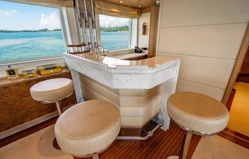 An interior wet bar onboard charter yacht ARTEMISEA, three cream stools surround the bar adjacent to large windows overlooking the sea