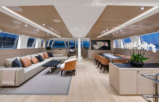 Interiors onboard charter yacht ATLANTIKA, with lounge area to port and dining set up to starboard, surrounded by large windows