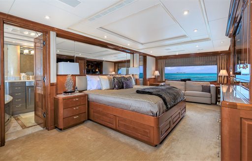 Owner's cabin on a superyacht, with bed in the centre of the space in front of a flat-screen TV, window in background looking out over the Caribbean, and door leading to en-suite