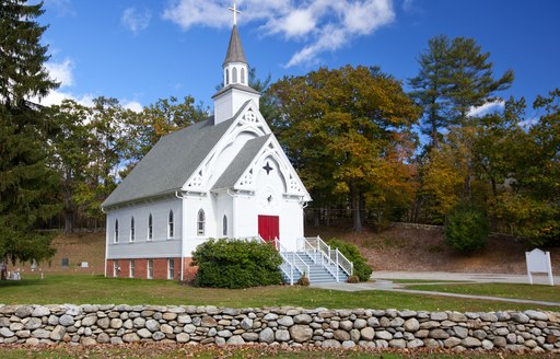 Small white church surrounded by green foliage in New England