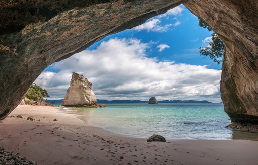 Coromandel Cove in New Zealand, view through arched rock to beach and clear sea