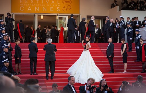 Woman in white ballgown on top of steps at Cannes Film Festival at Palais des Festivals, with guests surrounding