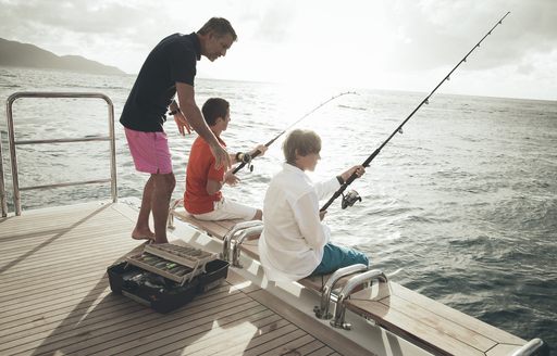charter guests fish on edge of swim platform on board motor yacht MEAMINA 