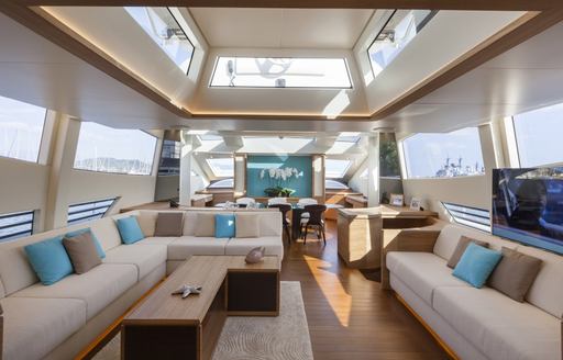 Overview of the main salon onboard charter yacht 55 FIFTYFIVE, extensive lounge area in the foreground with ample glazing to port and starboard