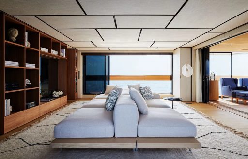 Spacious seating area onboard charter yacht LA LA LAND, sofas backed against each other in center with bookshelf and large windows in the background
