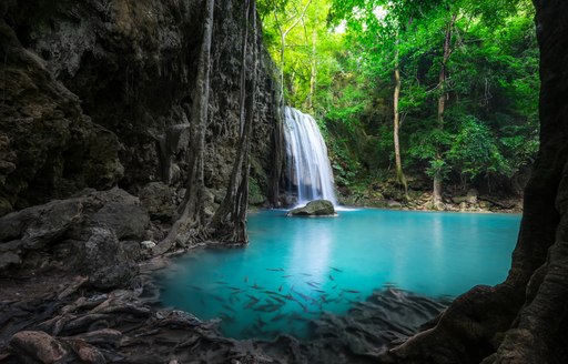a waterfalls cascades into aqua waters in a hidden lagoon in thailand