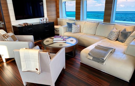 Interior lounge area onboard charter yacht W, white plush seating surrounds a coffee table with large windows aft