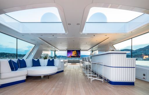 Overview of the sun deck onboard charter yacht CORAL OCEAN, wet bar to starboard with a white sofa to port and television aft