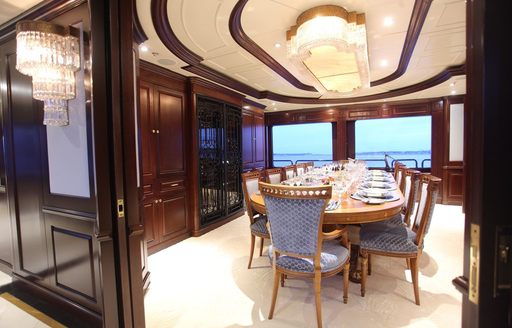 Interior dining area onboard charter yacht PURPOSE, long table set for a meal adjacent to large windows