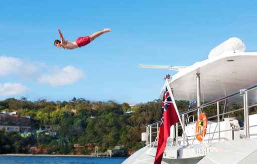 man dives into water from the deck of a luxury superyacht