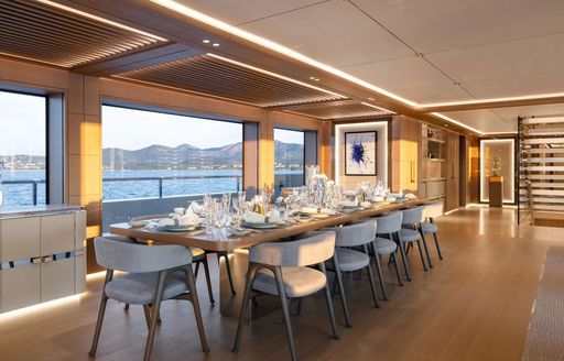 Dining area onboard charter yacht ALCHEMY. Long dining table with 12 chairs and wide windows in the background