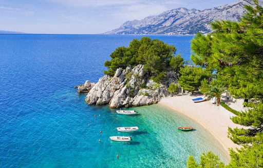 Secluded beach and anchorage in Croatia, with white sand and lush pine trees in foreground and mountain terrain in background