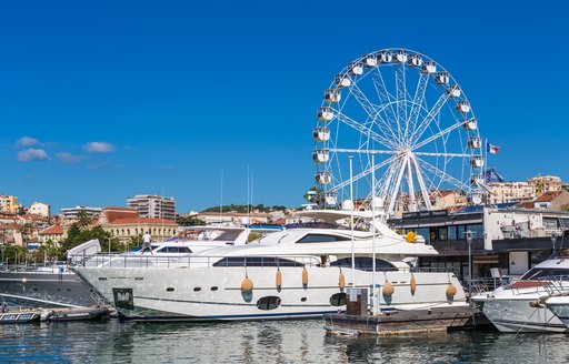 A motor yacht charter berthed in Cannes with a large ferris wheel in the background