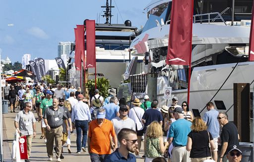 Many visitors at the Miami International Boat Show walking along the docks with motor yachts berthed to the right-hand side