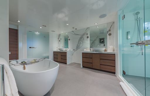 A private bathroom attached to the master cabin onboard charter yacht BIG SKY, a bath tub to port with separate shower cubicle starboard and sinks in the background