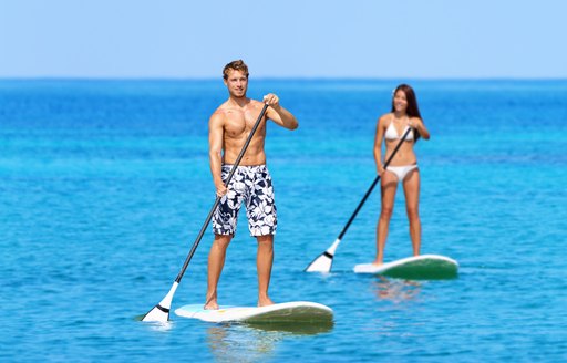 Man and woman stand up paddleboarding on ocean. Young couple are doing watersport on sea. Male and female tourists are in swimwear during summer vacation.
