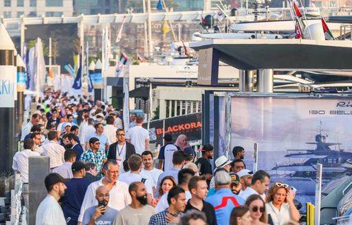 Many visitors at the Dubai International Boat Show walking along the docks beside displaying motor yachts