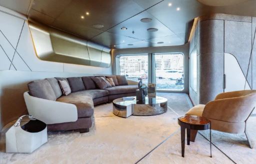 Interior lounge area onboard charter yacht THIS IS IT, curved sofa faces a brown armchair and extensive glazing