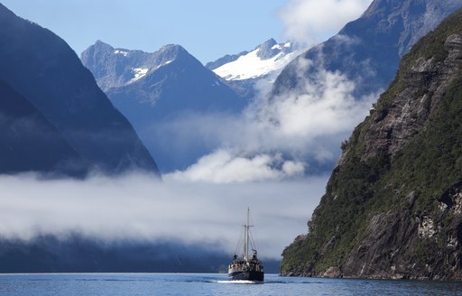 Boat cruising on water of Milford Sound - with mountainous background and snow peaks
