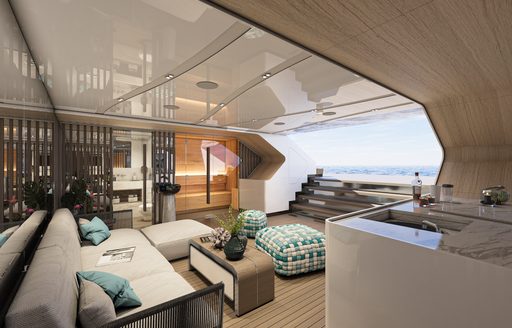 Overview of the beach club onboard charter yacht Eternal Spark, plush seating with a coffee table and sink in the foreground, with open air access to the exterior.