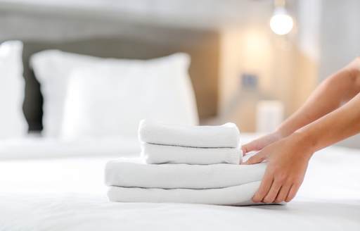 White towels small and large being laid on a white linen bed