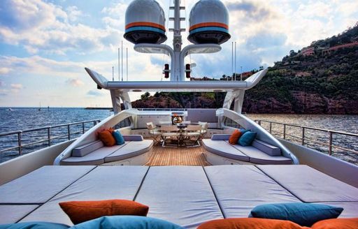 Sundeck on superyacht AURELIA, with sunpads in foreground and dining in background, with views over the French island of Corsica visible in the distance