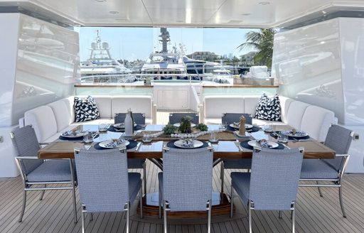 Alfresco dining set up onboard charter yacht SPORT, long table surrounded by eight upholstered chairs, with other yacht rentals berthed in the background