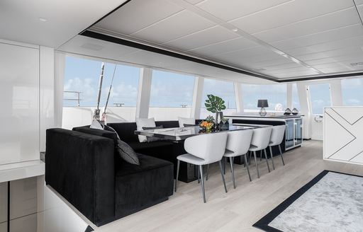 Interior dining area onboard charter yacht ABOVE & BEYOND, long table with plush black seating and white chairs, surrounded by large windows